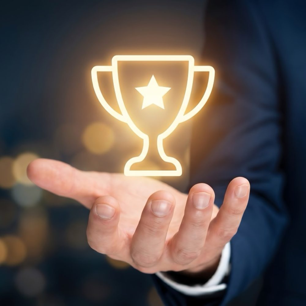 A modern conceptual image depicting a professional hand presenting a glowing golden digital trophy icon, symbolizing business success, corporate achievement, and excellence. This aspirational visual is perfect for marketing campaigns, motivational content, employee recognition, and illustrating future goals in presentations and reports.